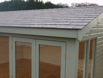 Close-up of a garden building roof finished with overlapping grey slate-effect tiles.